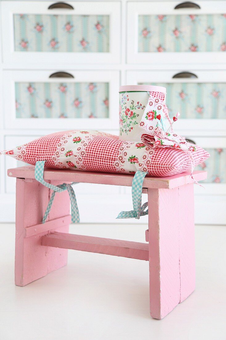 Romantic cushion with pattern of roses tied to pink, vintage stool and matching tin