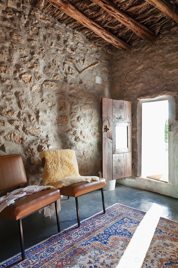 Braune Lederstühle vor Natursteinwand, im Hintergrund offene Tür und Lichteinfall auf Teppich