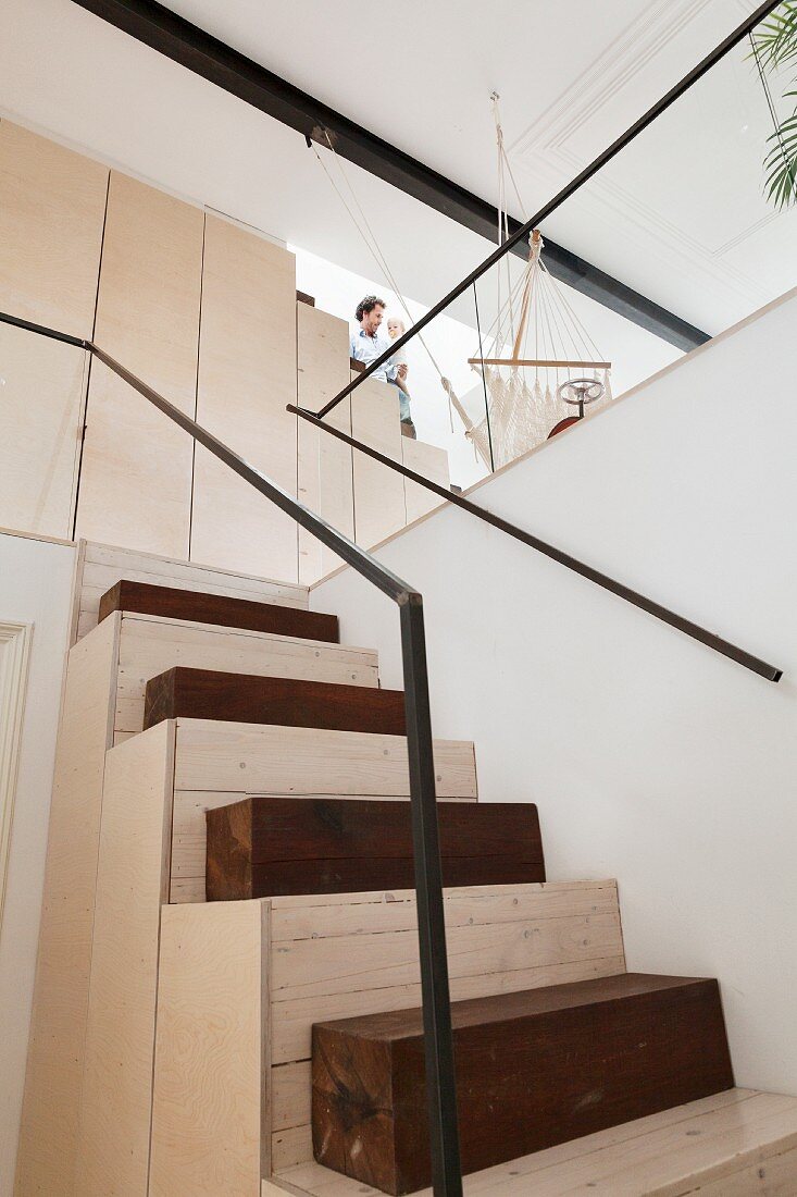 Massgefertigte Treppe aus hellem Holz und dunklen Vierkanthölzern, seitlich minimalistisches Geländer und Handlauf aus Metall