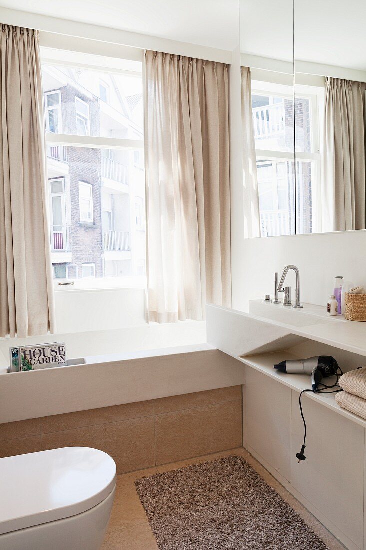 Modernes, helles Bad, massgefertigter Waschtisch neben vor Fenster eingebauter Badewanne