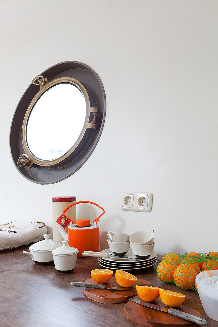 Oranges and crockery on surface below porthole window