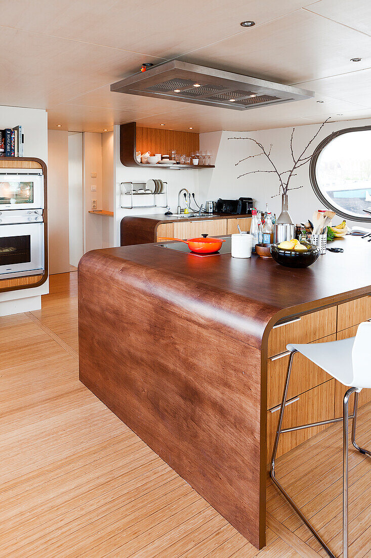 Island counter with curved wooden body in open-plan kitchen of houseboat