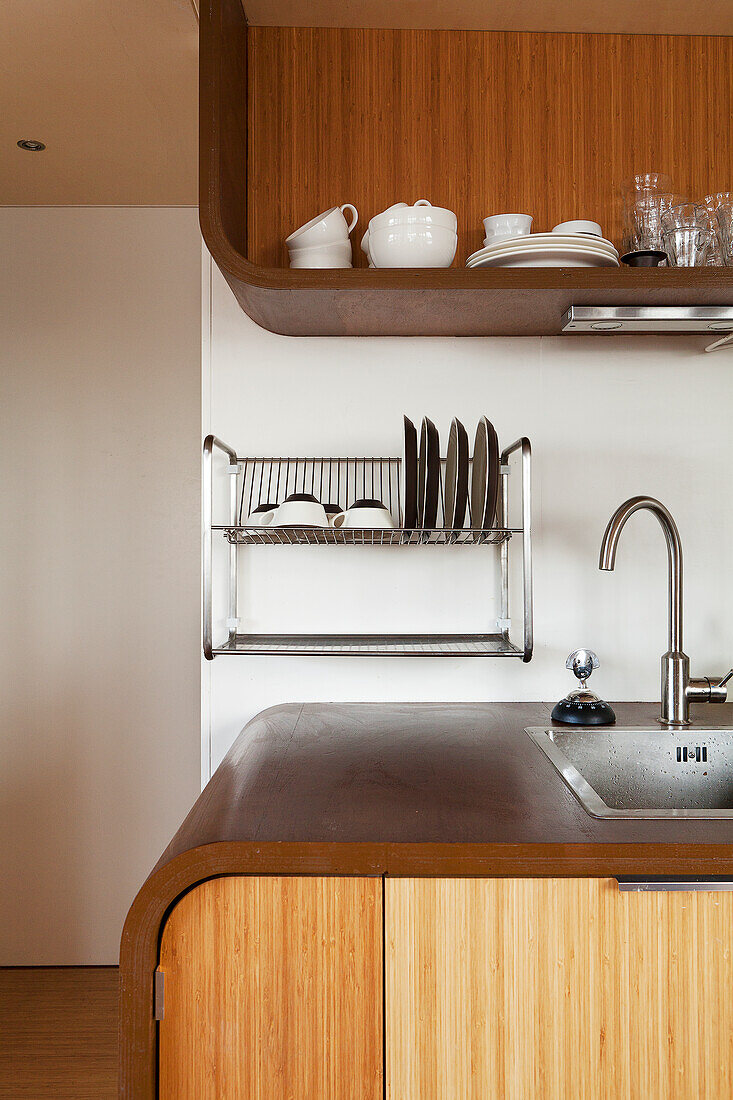 Sink integrated into counter with rounded wooden body with wall-mounted dish rack in background