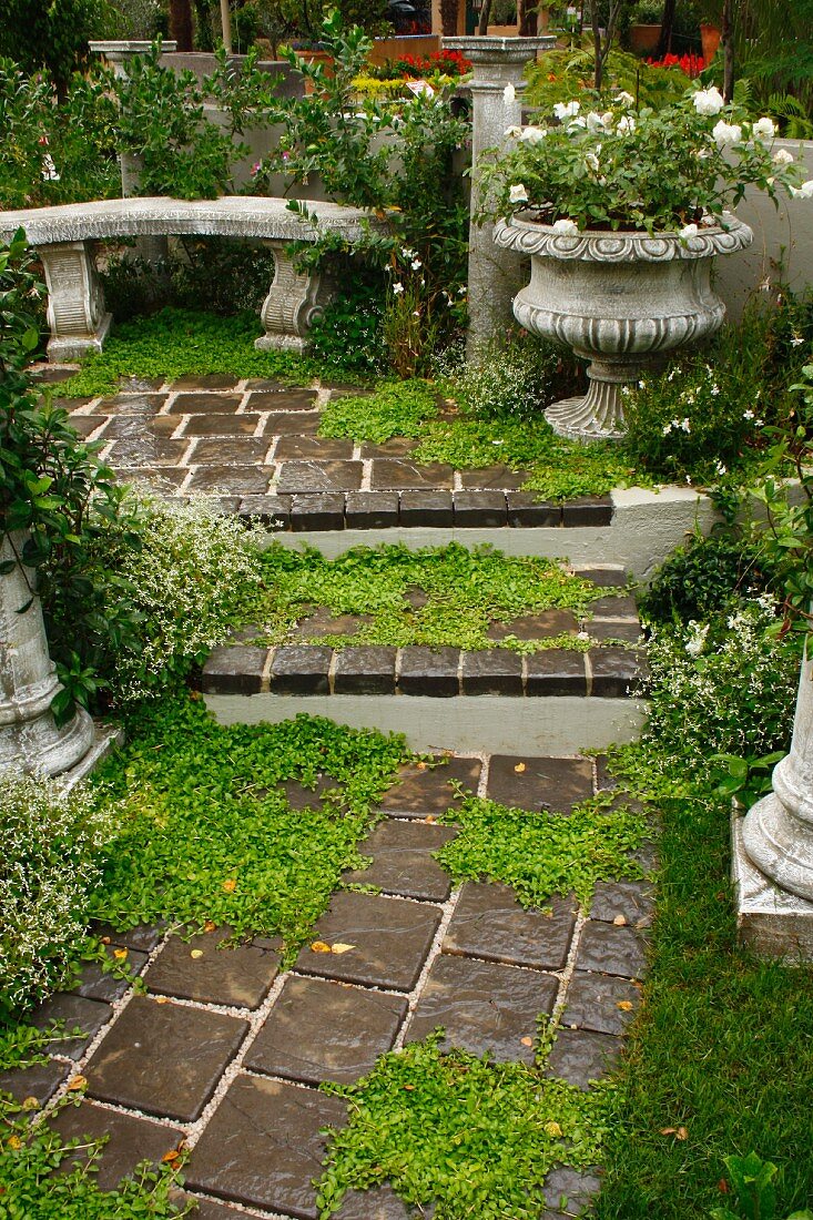 Treppe im Garten zu Sitzplatz mit antiker Steinbank, bepflanztem Pokal & niederigen Säulen