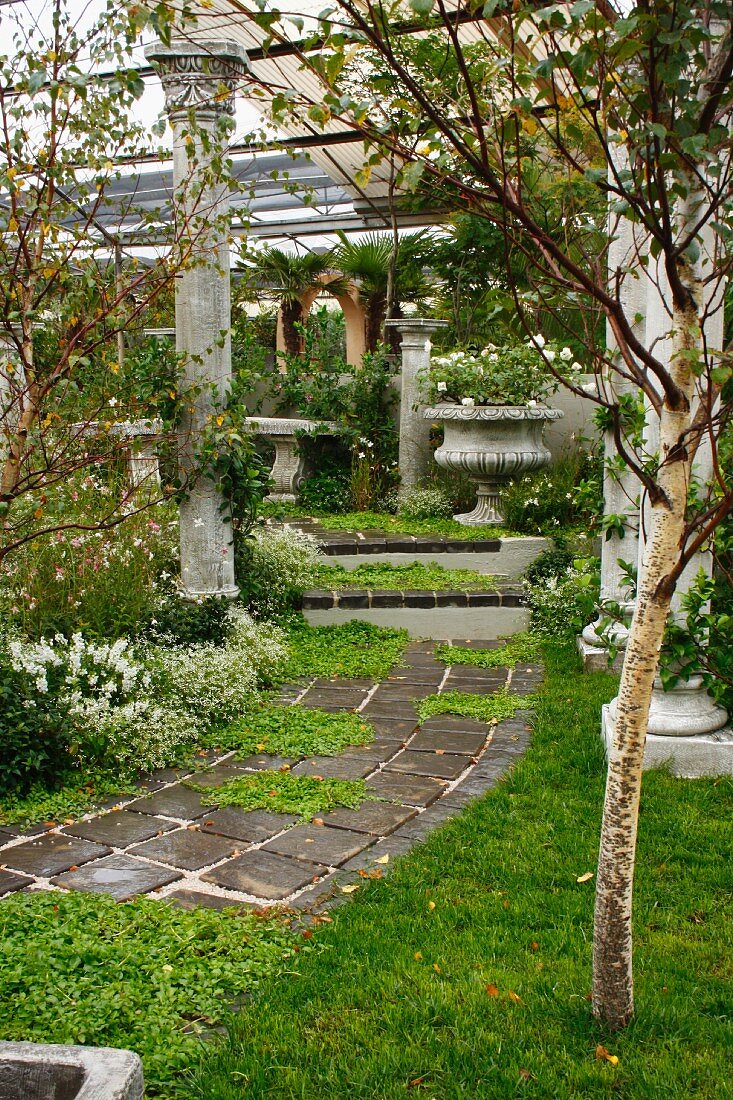 Antique columns lining path and steps leading to stone bench in seating area with planted urn