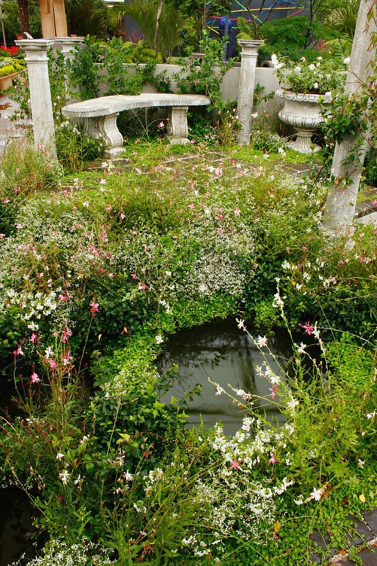 Kleine dicht bepflanzte Wasserteiche neben erhöhtem Sitzplatz mit antiker Steinbank & Säulen