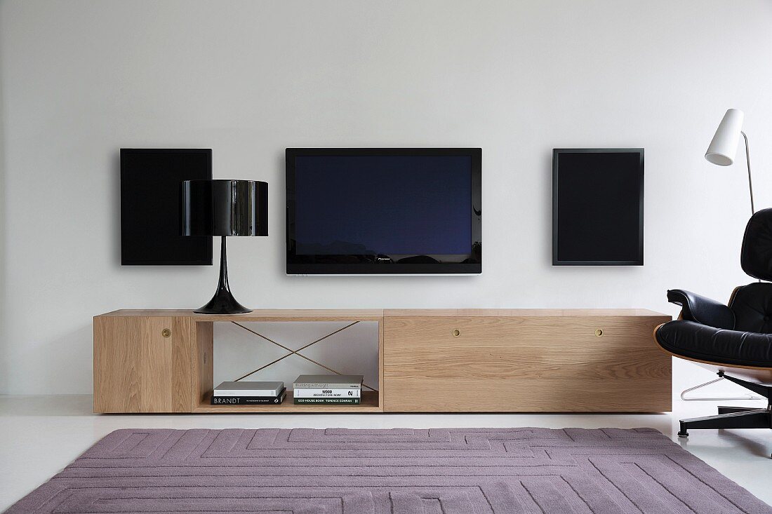 Table lamp on designer sideboard below speakers and flatscreen TV on white wall