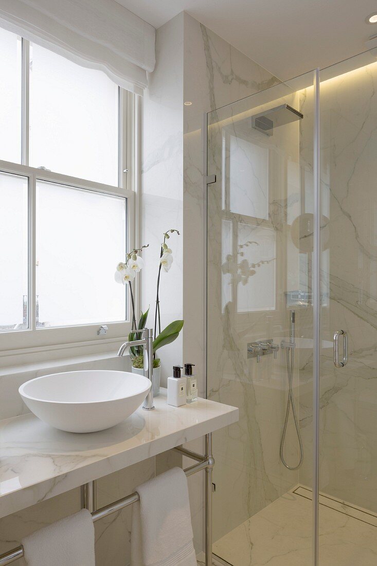 Elegantes Bad mit weißem Marmor, Duschbereich mit Glasabtrennung und Waschschüssel auf Marmorplatte
