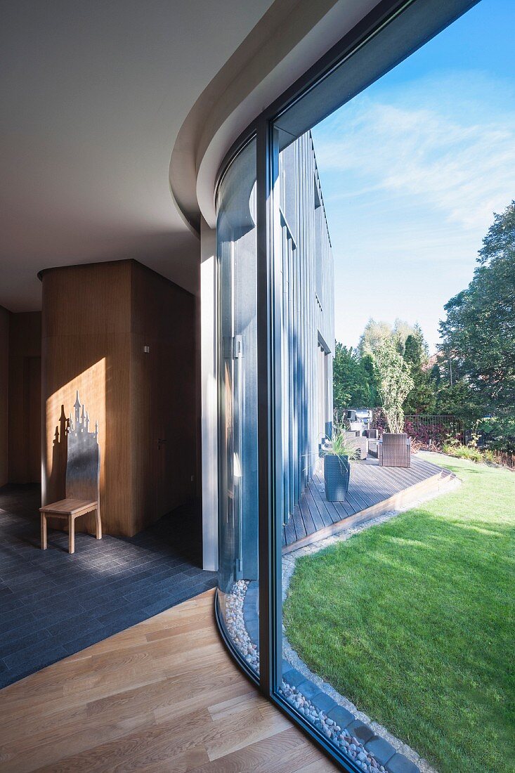 Gebogene Vollverglasung mit Blick in sommerlichen Garten eines Architektenhauses