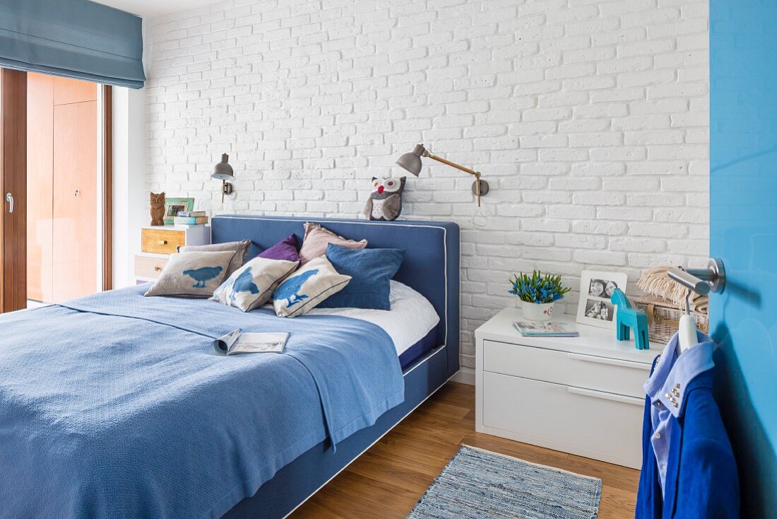 Doppelbett in Blautönen vor weiss geschlemmter Backsteinwand im Schlafzimmer