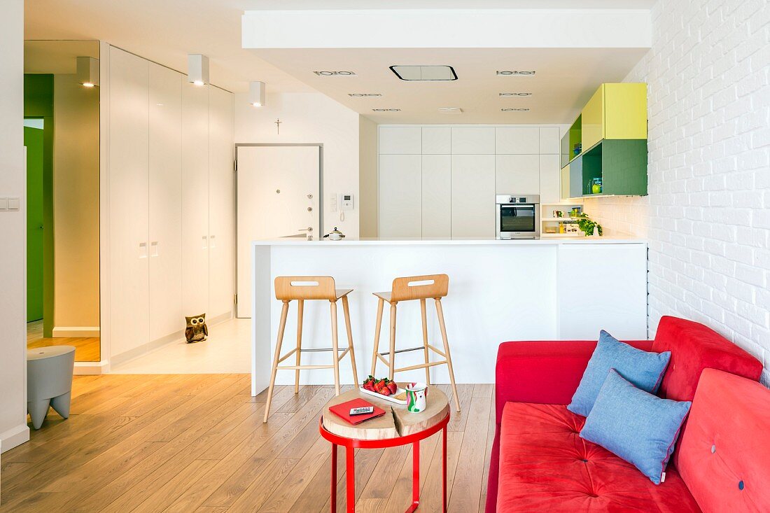 Rotes Sofa und weiße Einbauküche mit Frühstückstheke in offenem Wohnbereich
