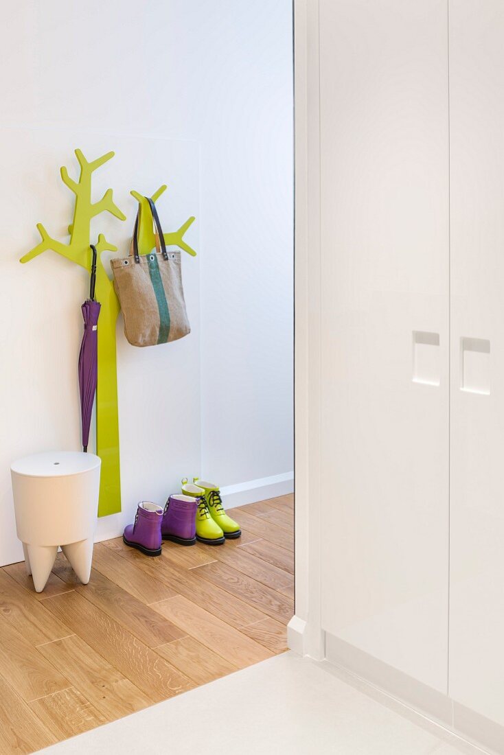 Green, stylised tree as coat rack and designer stool in hallway with fitted cupboards