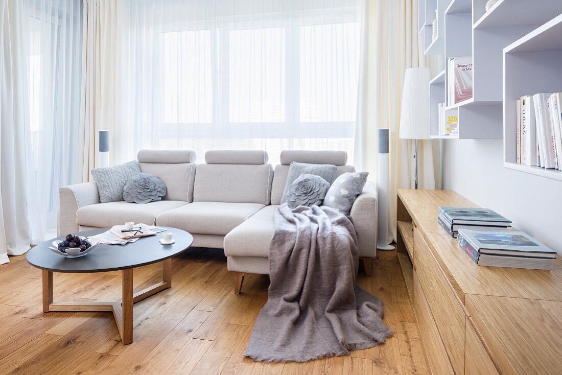 Helle Couch mit Coffeetable vor Fenster, neben eingebautem Sideboard aus hellem Holz