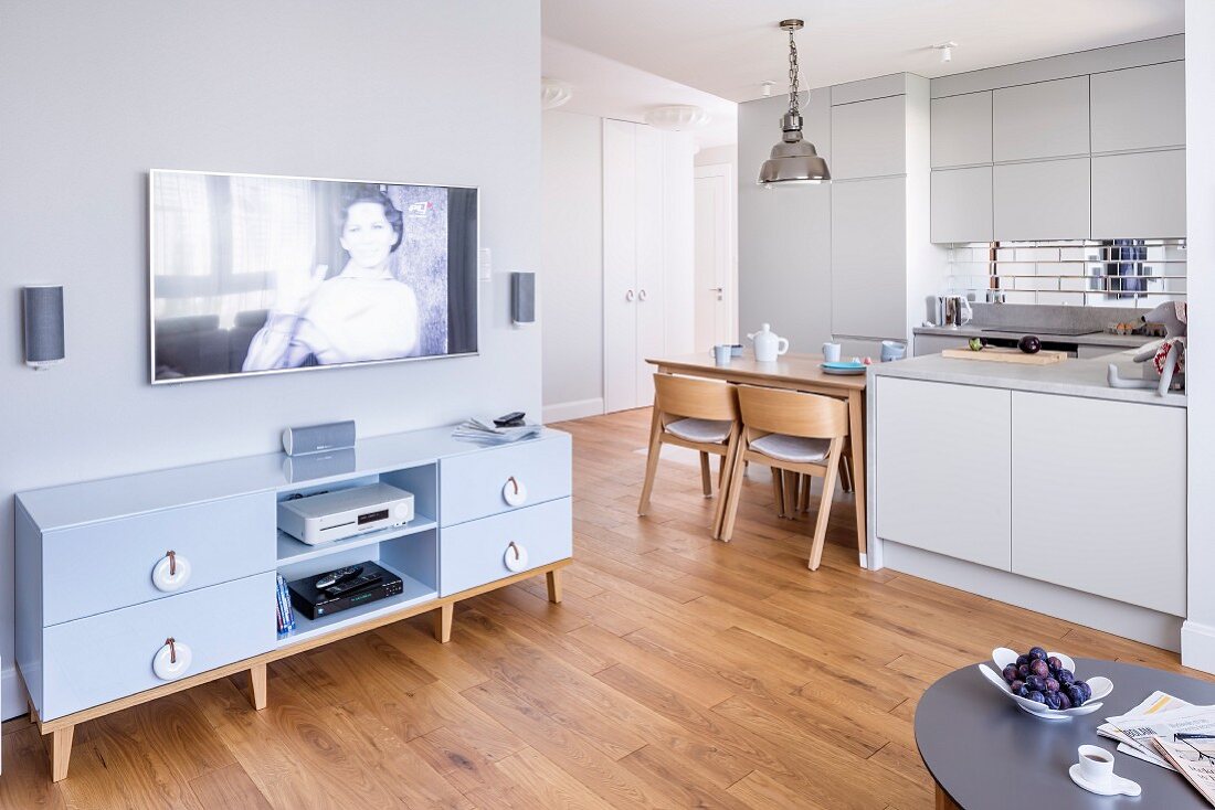 Flatscreen TV above media cabinet with fitted kitchen and integrated dining area in background