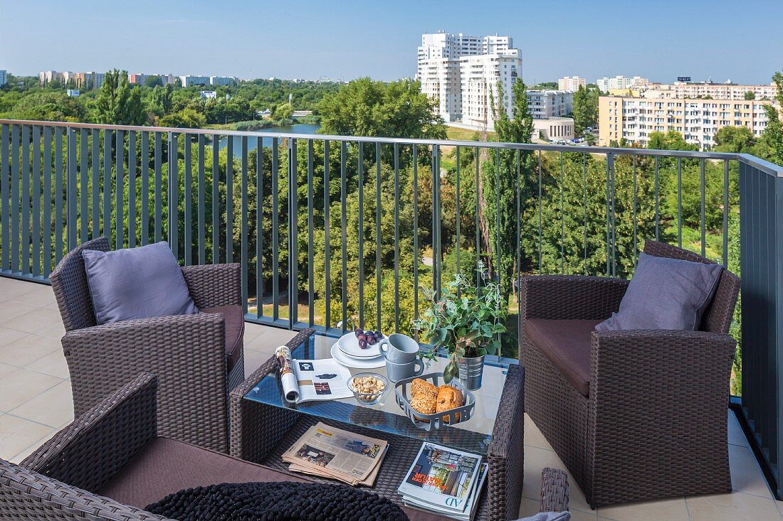 Outdoor-Möbel aus Kunstrattan auf Balkon mit Blick über Parklandschaft und Hochhausanlage