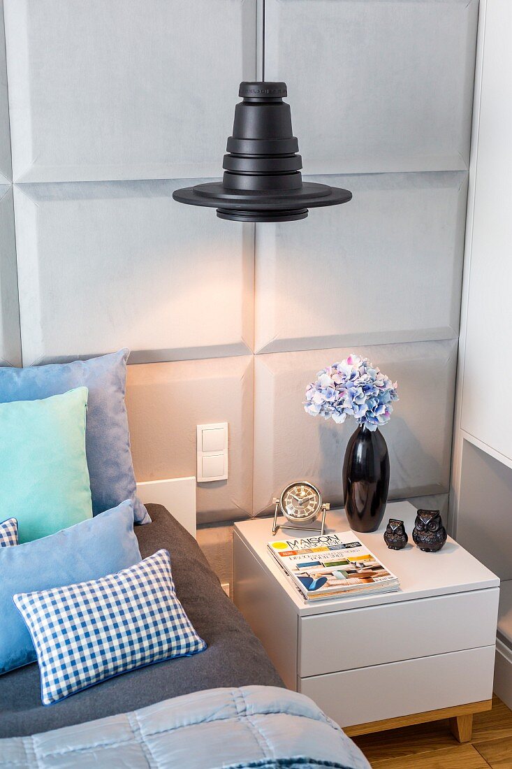 Black pendant lampshade above bedside cabinet against bedroom wall with panelled structure
