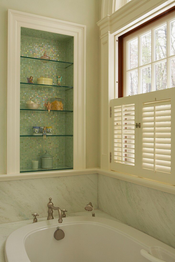 Elegant, country-house bathroom with marble cladding; ornaments on glass shelves in niche with shimmering mosaic tiles