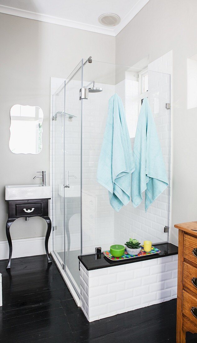 Shower cubicle with masonry shelf and white sink on old-fashioned, black table