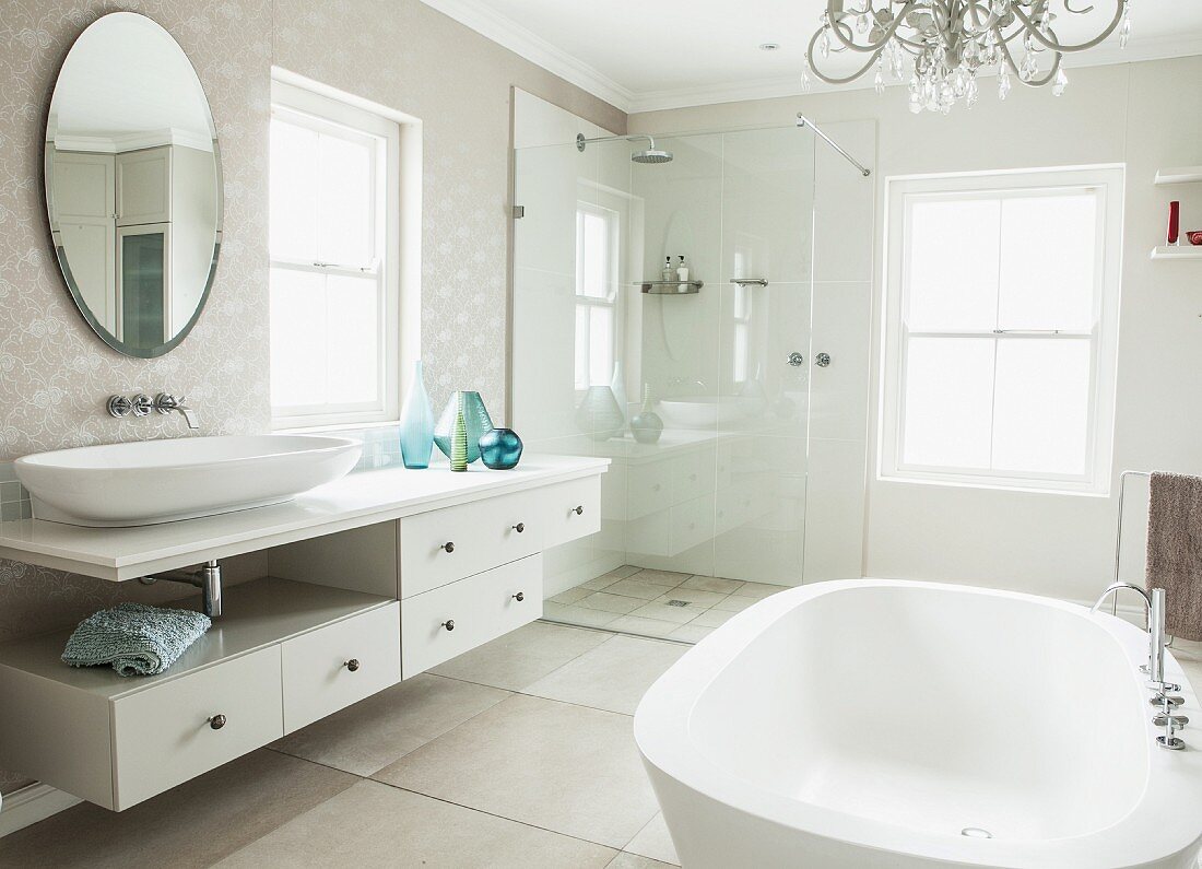 Elegant bathroom with free-standing bathtub, long washstand, oval mirror and glazed shower in corner