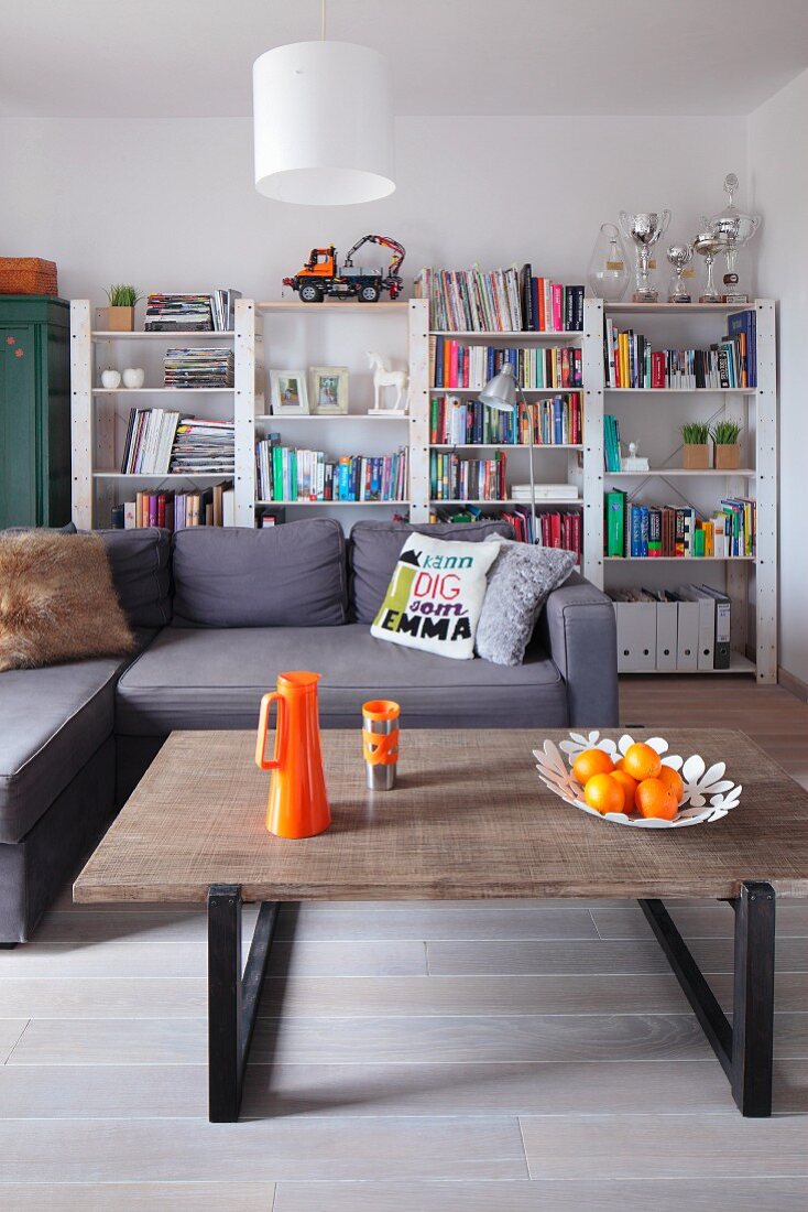 Moderner Coffeetable mit orangefarbenen Accessoires, Eckcouch und weiss lackiertes Bücherregal