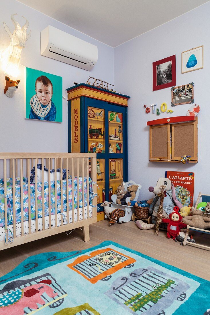 Rug with animal motifs, cot and soft toys on painted wardrobe in cheerful, bright child's bedroom