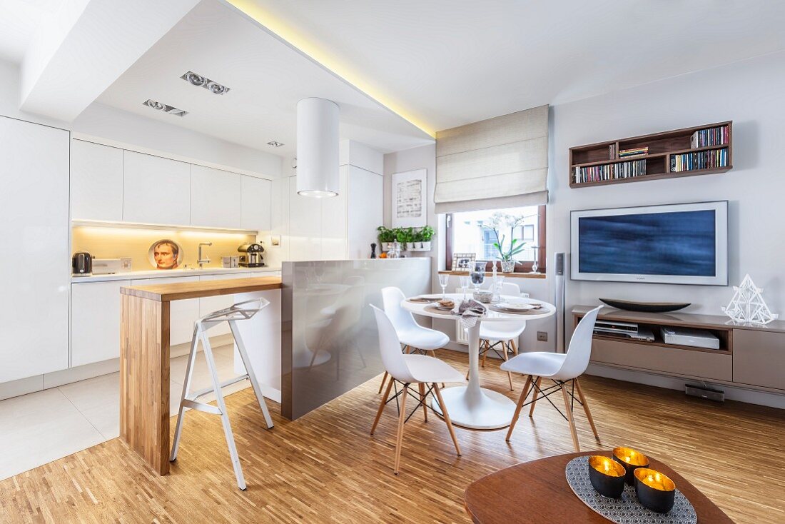 Classic dining area in front of open-plan, white fitted kitchen with engineered wood counter