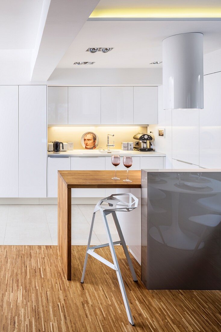 Designer bar stool at kitchen counter with solid-wood top in front of white fitted kitchen
