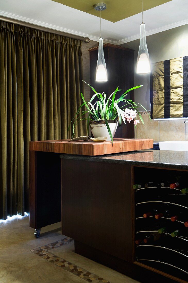 Island counter with integrated wine rack and swivelling kitchen trolley; pendant lamps above houseplant