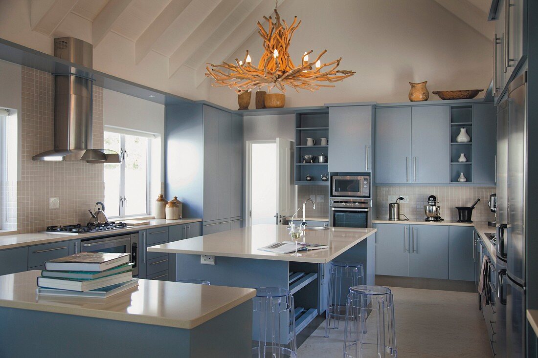 Moderne Küche mit Stein-Arbeitsplatten und und hellblauen Schrankfronten, über Mittelblock Kronleuchter aus Treibholz