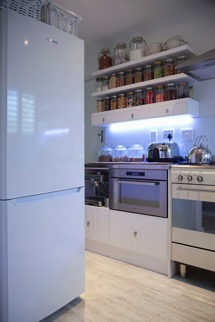 weiße Kühlschrankkombination, gegenüber Küchenzeile und Regalböden an Wand mit Aufbewahrungsgläsern