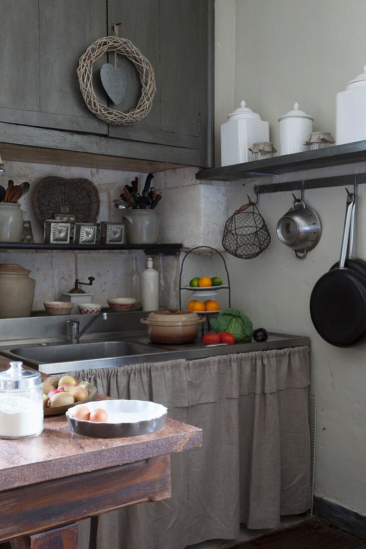 Mediterrane Küche mit vielen Regalen für nostalgische Aufbewahrungsgefäße, an der Spüle hängt ein Vorhang aus Leinen