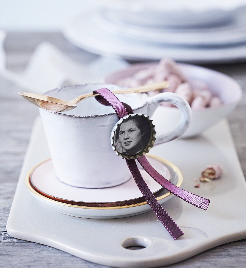 In Kronkorken eingeklebtes, altes Foto als Tischkärtchen an Kaffeetasse drapiert