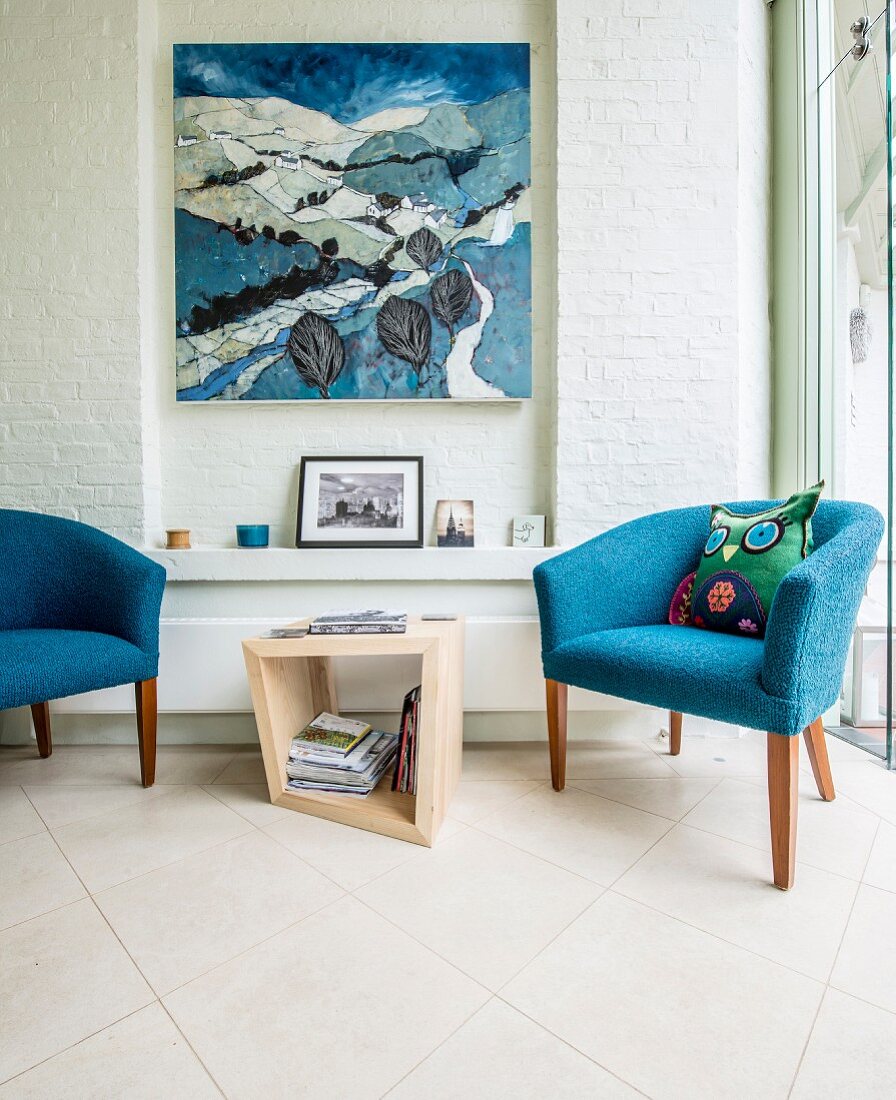 Blue fifties' armchairs flanking side table in front of artwork in narrow niche