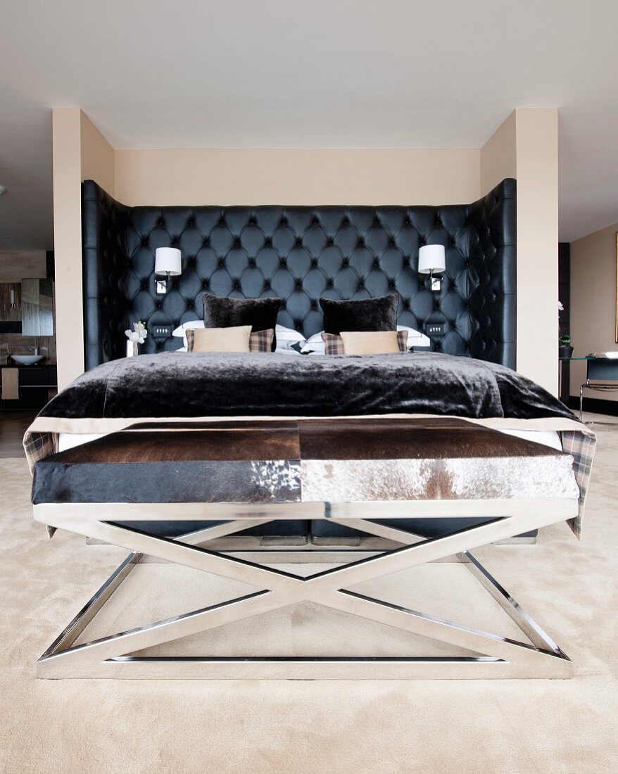Bed with black upholstered headboard and chrome bench with animal-skin cover in masculine bedroom