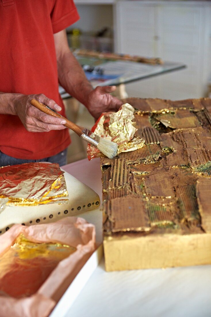 Person beim Vergolden eines Kunstobjekts in Künstlerwerkstatt