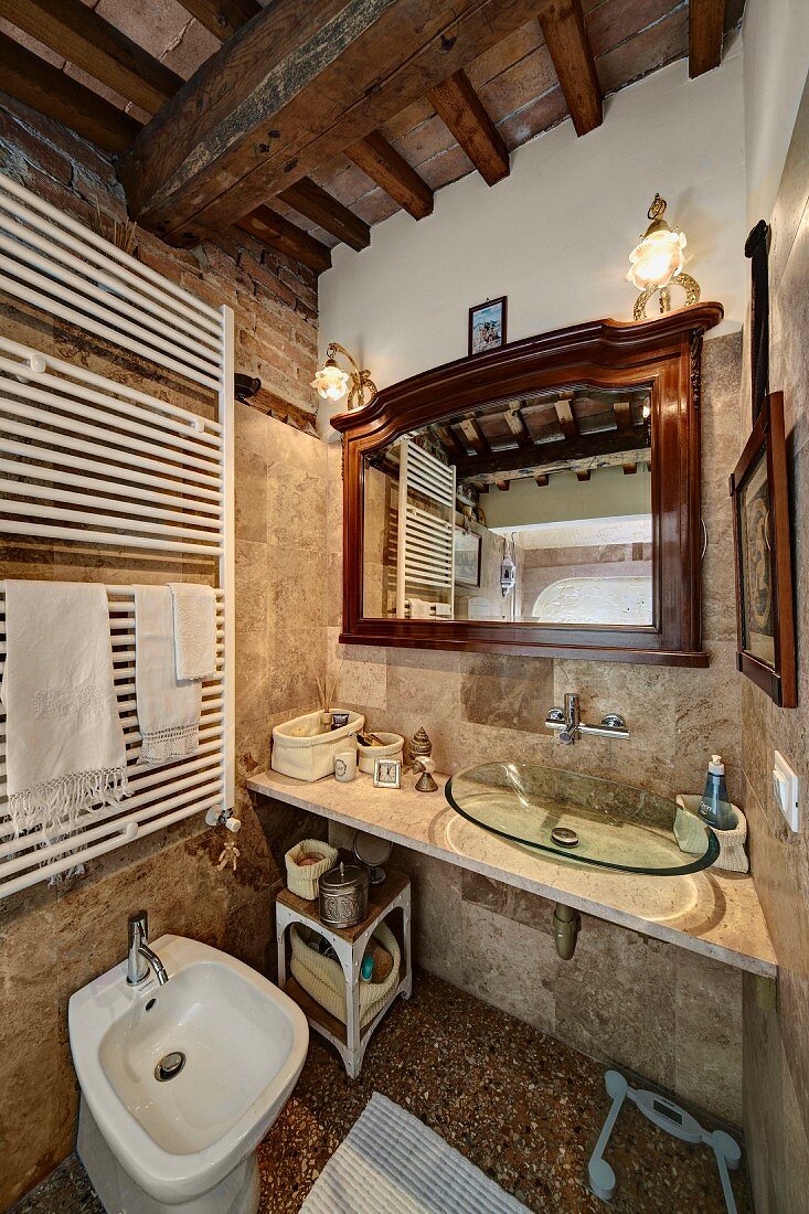 Rustikales Bad mit Holzbalkendecke, Waschtisch mit moderner Glasschale als Becken, seitlich weisser Handtuchtrockner über Bidet