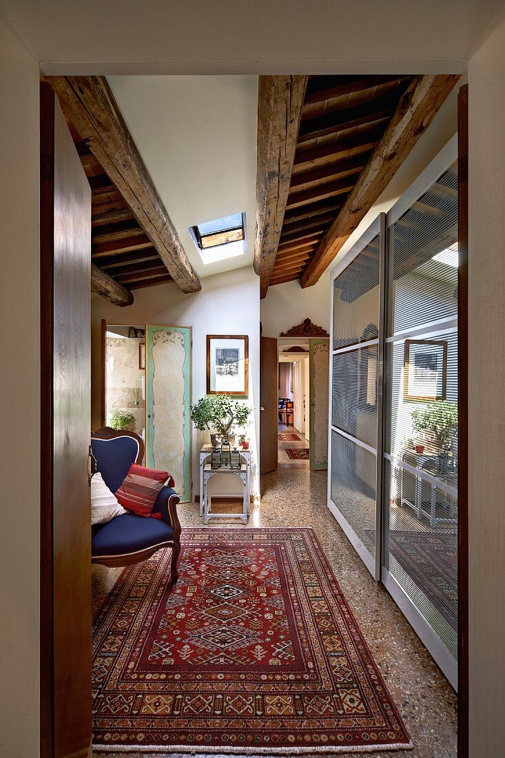 Antique armchair, Oriental rug and modern cupboards with sliding doors in foyer leading to long, narrow corridor