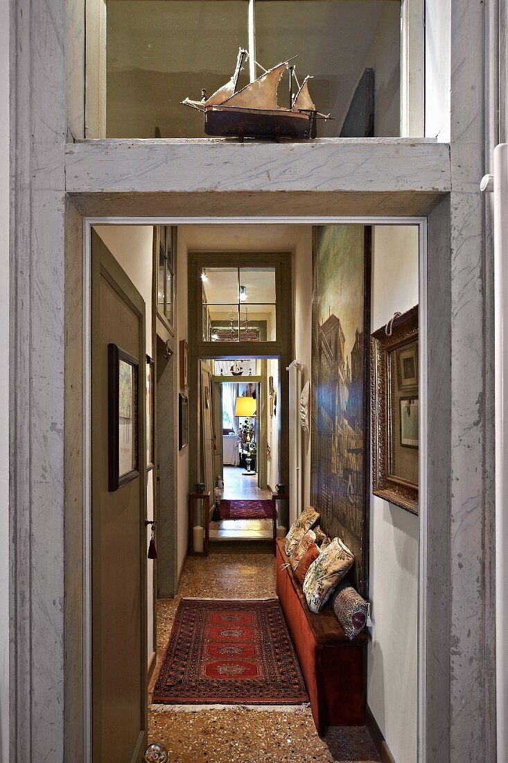 View through open door down long, narrow hallway with traditional ambiance and rug on terrazzo floor