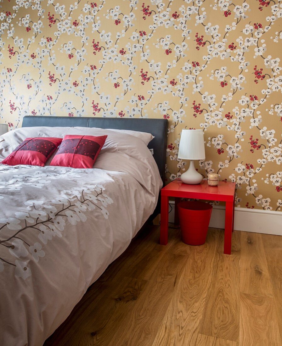 Elegantes Schlafzimmer mit asiatischem Flair, Satin Bettwäsche auf Bett, vor tapezierter Wand mit floralem Muster auf goldenem Grund