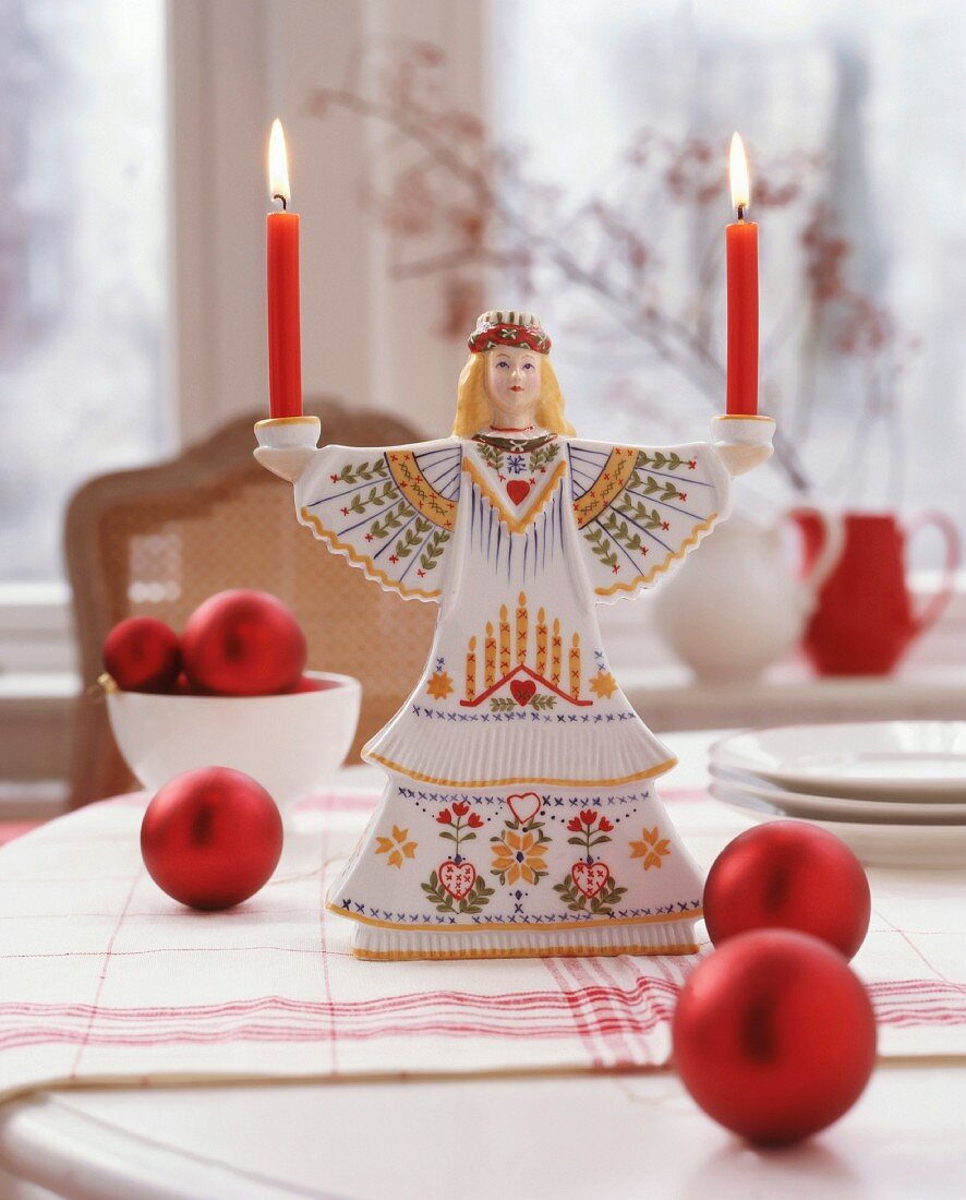 Skandinavische Lucia-Figur als Kerzenständer auf Tisch mit roten Christbaumkugeln