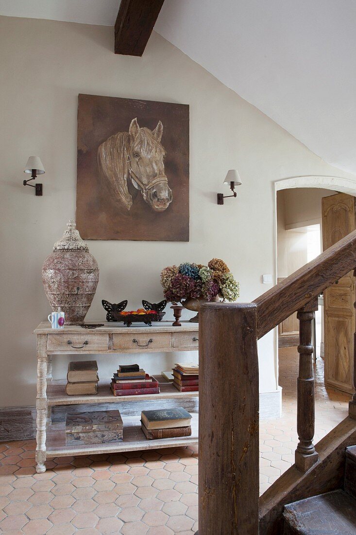 Console table, painting of horse and old wooden staircase in rustic-style hallway