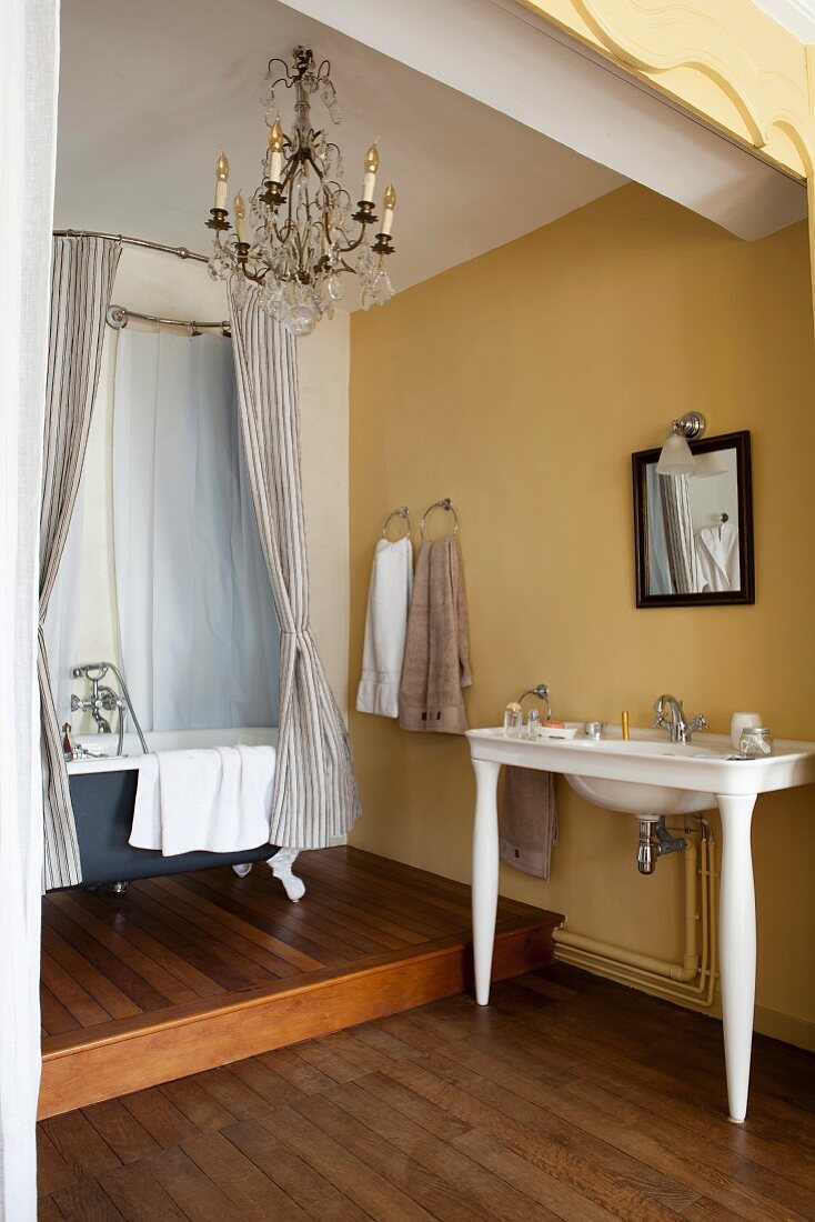 Nostalgisches Badezimmer mit gelben Wänden, Holzboden, Waschtisch und freistehender Badewanne auf Podest