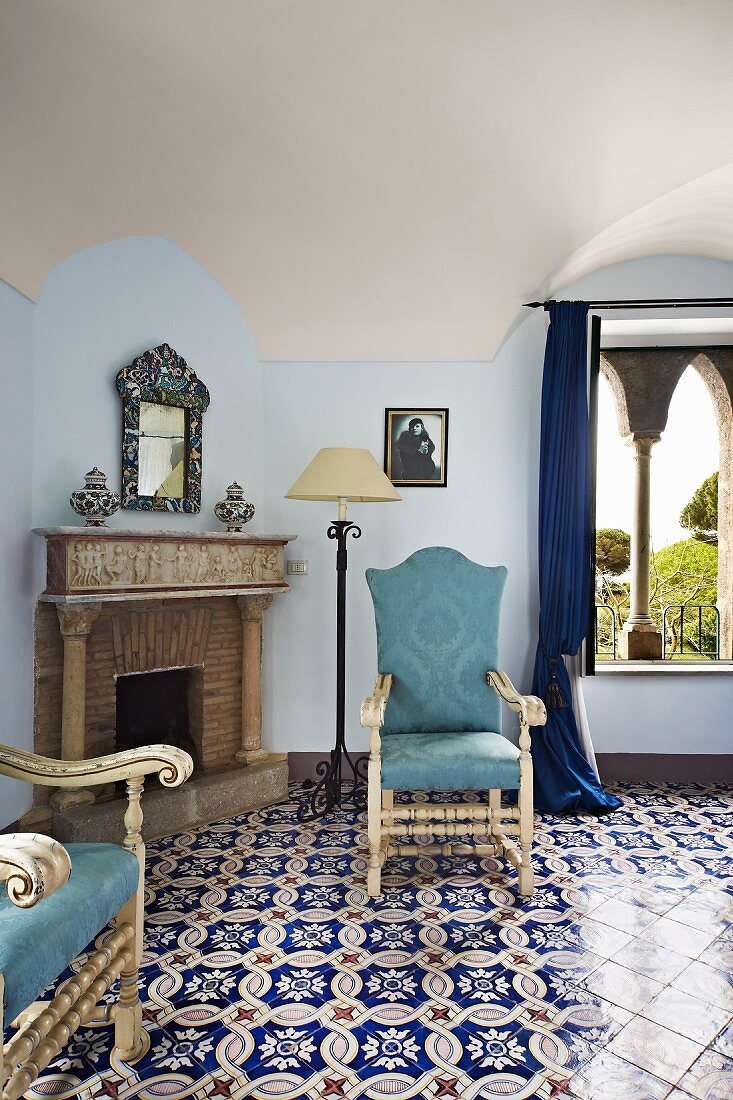 Elegant, ornate floor tiles and chairs with light blue upholstery in front of open fireplace (Villa Cimbrone Hotel)