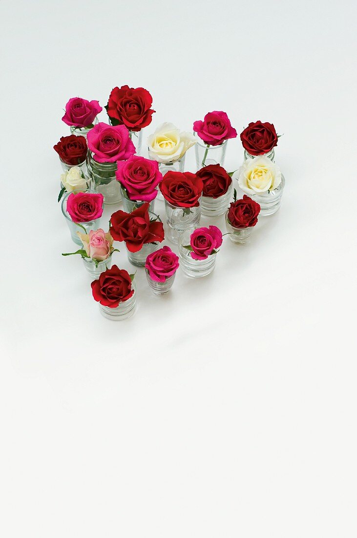 In Herzform aufgestellte Gläschen mit Rosenblüten als Tischdeko für den Valentinstag