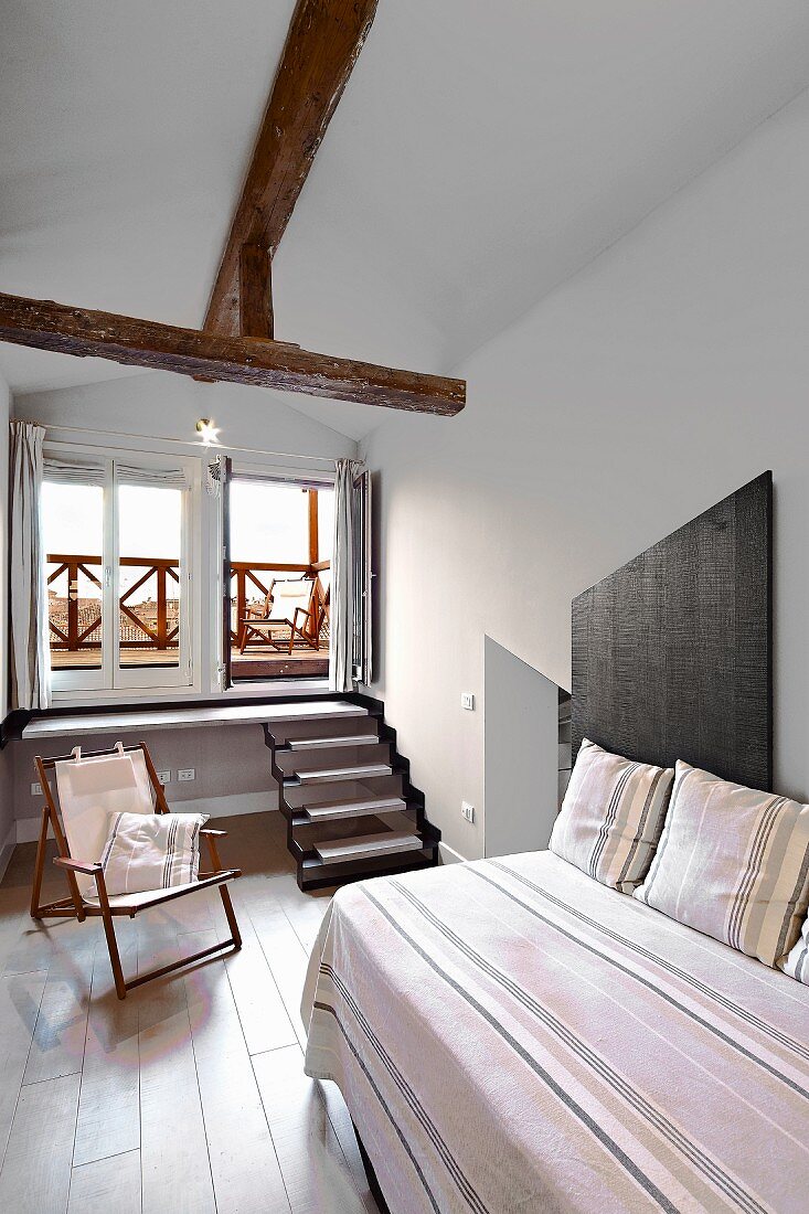 Renoviertes Zimmer mit Einzelbett, gestreifte Tagesdecke und Kissen aus gleichem Stoff, im Hintergrund Treppe vor Fenster mit Balkon