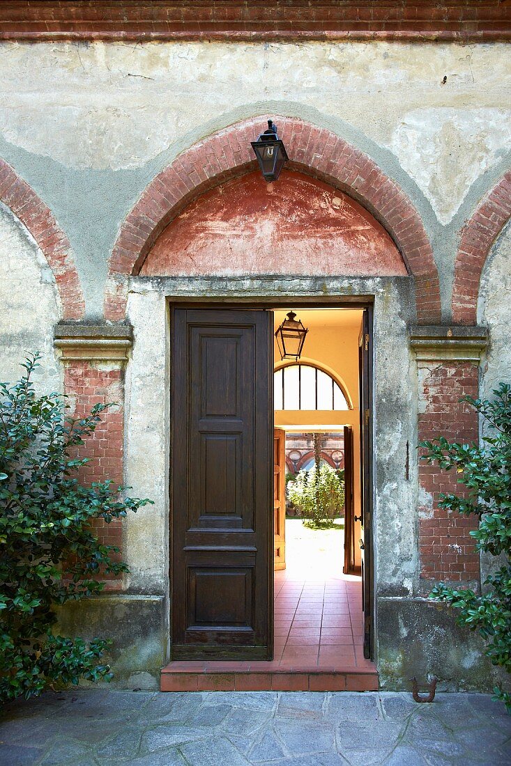 Halboffene Flügeltür mit Blick in den Innenhof eines italienischen Herrenhauses mit abgeblätterter Fassade