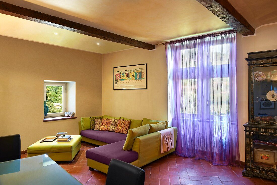Italian, designer sofa and ottoman in green and purple, terracotta floor tiles and purple, voile curtain