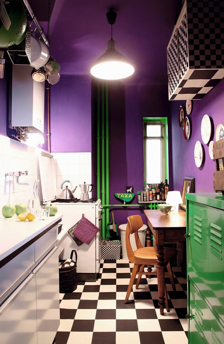 Violette Wände, grüner Metallschrank und Heizungsrohre in kleiner Küche mit Schachbrettmusterboden