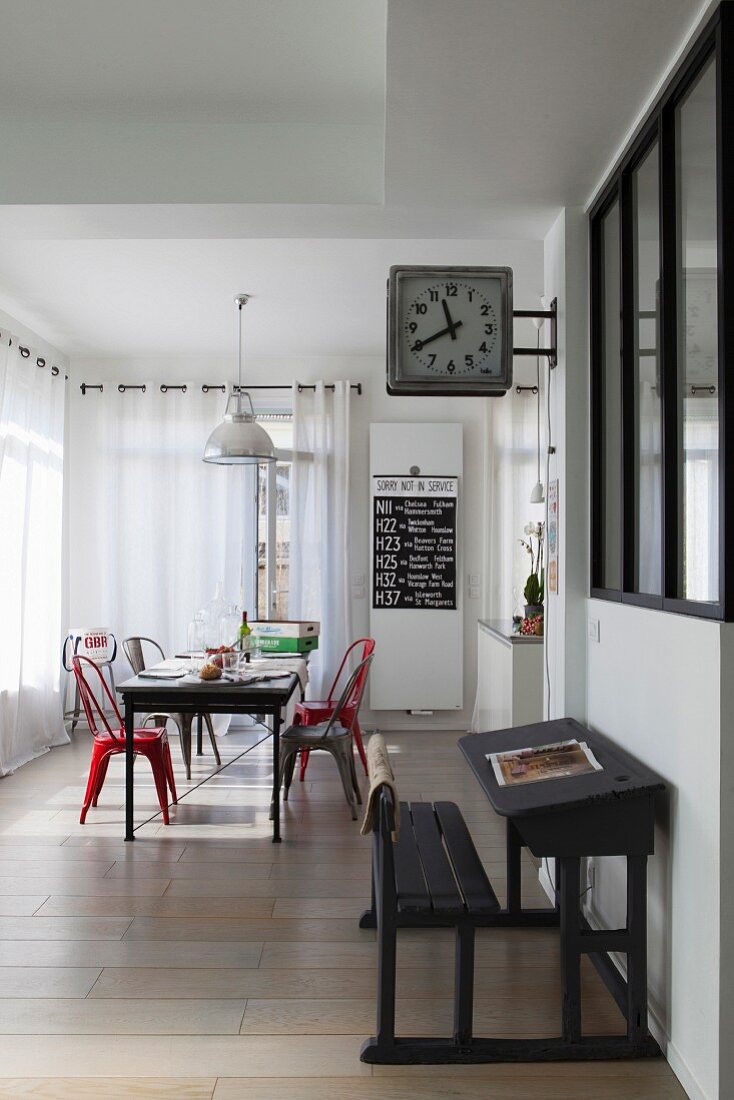 Dining area and decorative station clock above antique school desk in elongated, open-plan interior