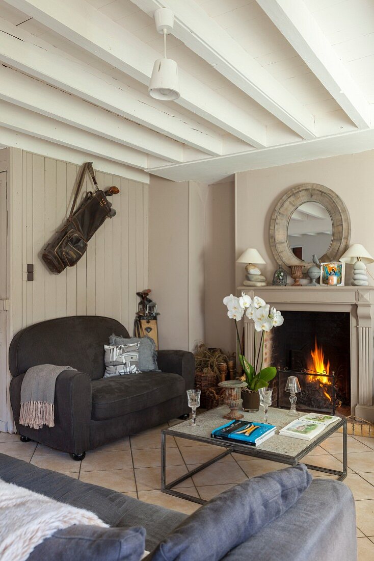 Wohnzimmer mit offenem Kamin, grauen Sofas und Sichtbalkendecke